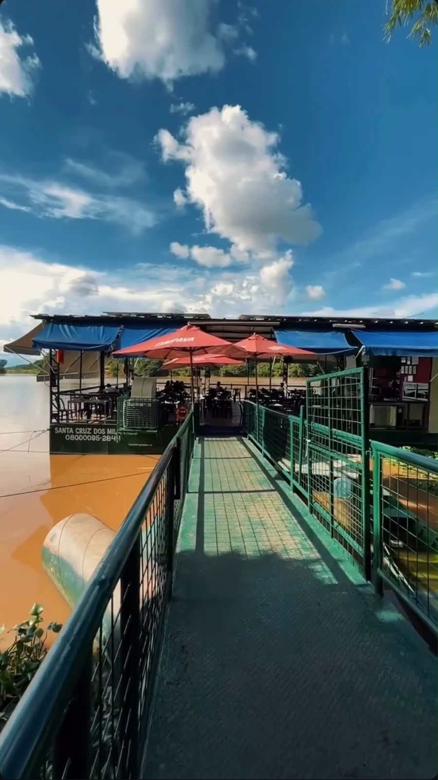 Passarela de acesso ao deck flutuante, com guarda-sóis e mesas sobre o rio