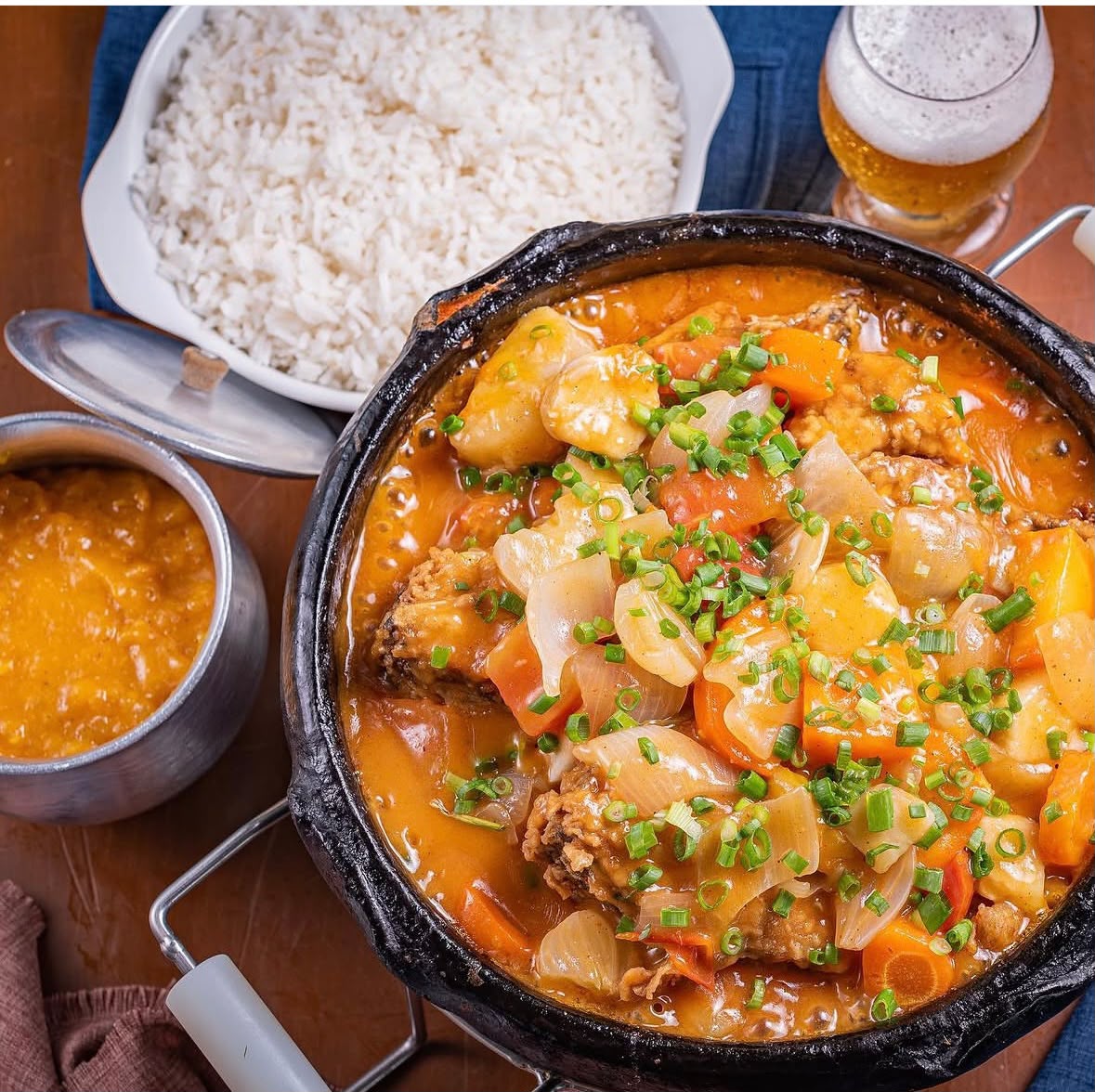 Peixada servida na panela de barro com legumes, ao lado de arroz branco e pirão