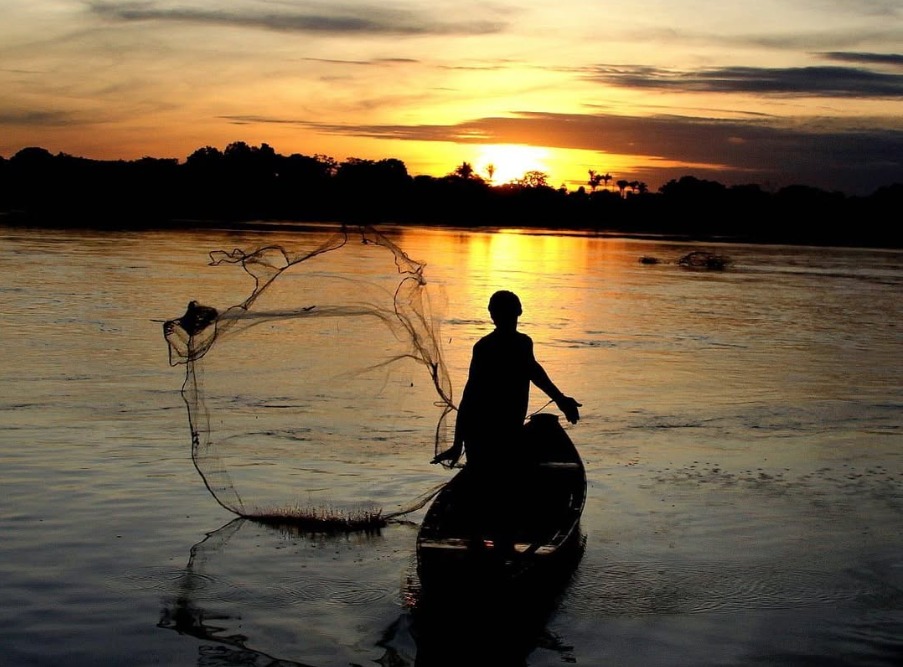Pescador jogando tarrafa no rio ao pôr do sol